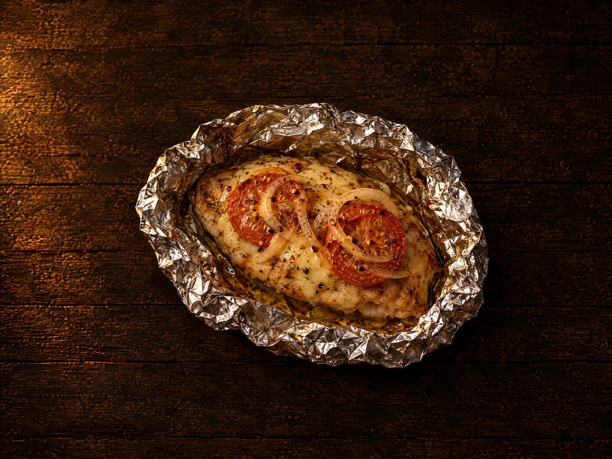 Filete de tilapia en papel aluminio abierto, con queso asadero, jitomate y cebolla
